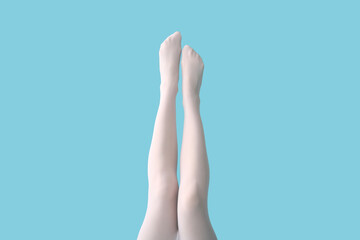 Legs of young woman in white tights on blue background