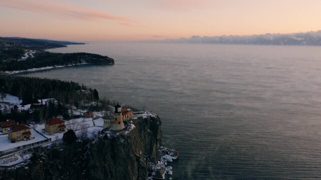 Wide aerial slide showing the proximity of Split Rock Lighthouse to the snowy North Shore forest and highway at sunrise.