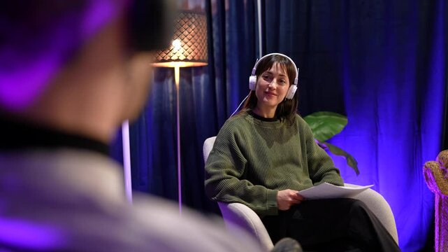 Content creator woman hosting a podcast and talking to a guest during a live streaming show in a modern recording studio with professional equipment for social media content creation