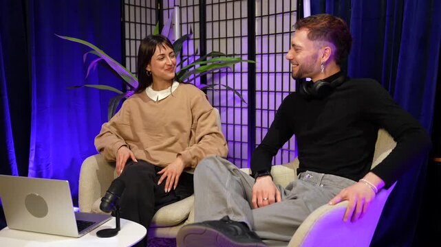 Cheerful male and female influencers celebrating the end of a successful live streaming podcast session in a professional recording studio by giving a high five and then hugging each other