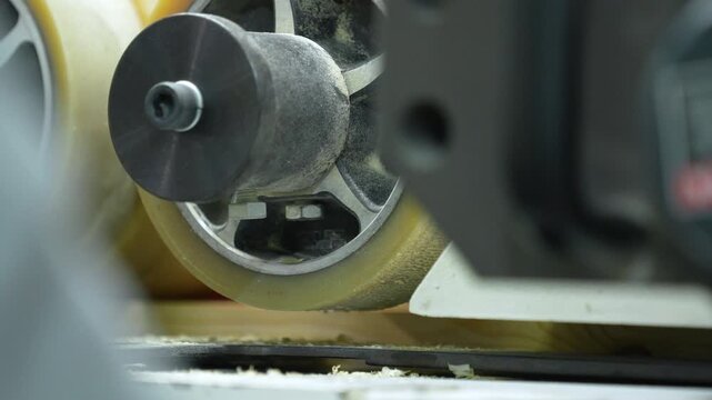 Extreme close up of heavy duty industrial roller feeding a wooden plank into a processing machine. Perfect for manufacturing, woodworking, and carpentry industry content.