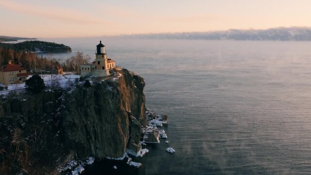 Aerial drone view of Split Rock Lighthouse on its iconic cliff over Lake Superior with winter sea smoke at dawn.