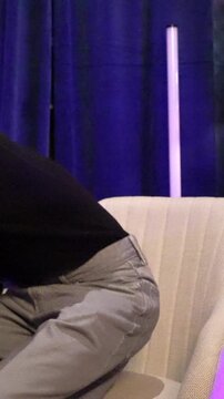 Young male influencer speaking and laughing while reading a script from his notes during an interview, sitting in a modern armchair inside a professional content creation studio