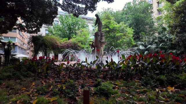 Gentle Panning Shot Capturing the Historic Decorative Water Fountain and Leafy Trees in Placa Gabriel Miro Park, Downtown Alicante, Spain.