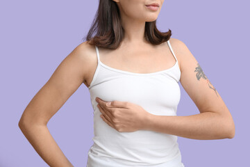 Fototapeta premium Young woman checking her breast on lilac background, closeup. Cancer awareness concept