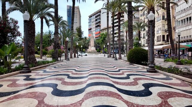 POV shot walking along the iconic Explanada de Espa&ntilde;a promenade's mosaic pavement towards the historic Monument a Canalejas in sunny Alicante, Spain.