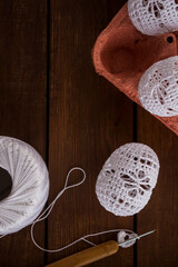 Vertical Easter background with handmade white crochet eggs in egg carton on rustic wooden table. Cozy spring decoration, natural textures, copy space.