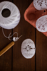 Vertical Easter background with handmade white crochet eggs in egg carton on rustic wooden table. Cozy spring decoration, natural textures, copy space.