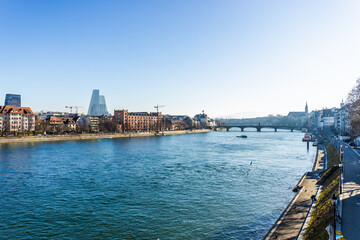 Scenic view of the Rhine river in Basel, Switzerland, featuring historic brick architecture on the riverbank under a bright blue sky.