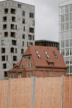 Urban residential architecture shows heritage house behind fence in Hamburg Germany with modern towers creating strong contrast in city growth scene