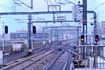 曇り空の下に広がる複雑な鉄道の線路と赤信号。日本の都市部における交通インフラの風景