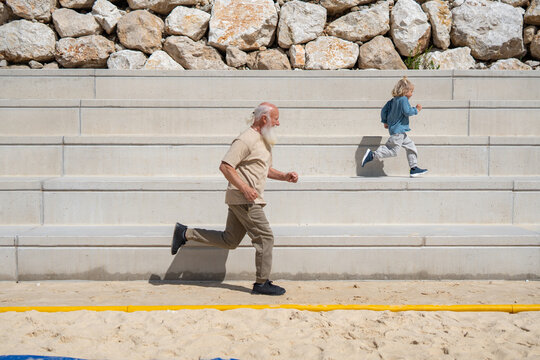 Energetic grandfather and young boy running up stone bleachers outdoors, showcasing intergenerational fitness, joy, and active lifestyle. Senior man and child exercising together in sunshine 