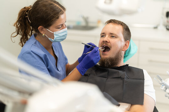Man sits anxiously in a chair at a dentist appointment. Client of a dental clinic came to treat his teeth. Female dentist carefully examines teeth before treatment