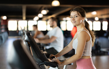 Fototapeta premium Young athletic woman working out on exercise bike in gym
