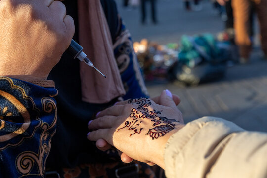Henna artist in the the iconic and famous Jamaa el Fna square, applying a design to a woman's hand with a syringe. Jamaa el Fna,Marrakech,Unesco hertage,Morocco