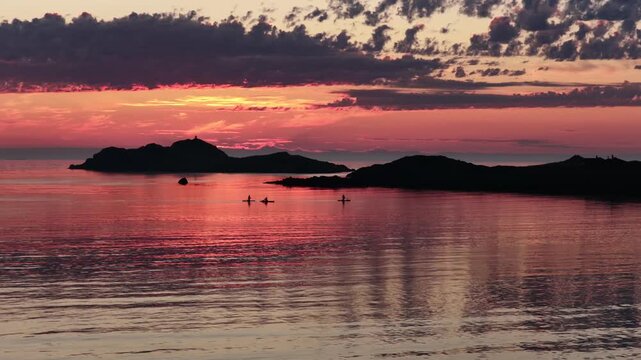 drone flight above sea at Ramberg beach, midnight sun in summer. 3 people on SUP board stand-up paddleboard enjoying sea and midnight sun in arctic Norway. Amazing nature, travel destination.