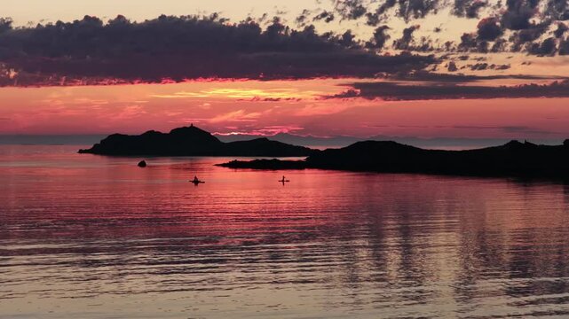 drone flight above sea at Ramberg beach, midnight sun in summer. 3 people on SUP board stand-up paddleboard enjoying sea and midnight sun in arctic Norway. Amazing nature, travel destination.