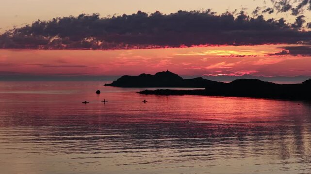 drone flight above sea at Ramberg beach, midnight sun in summer. 3 people on SUP board stand-up paddleboard enjoying sea and midnight sun in arctic Norway. Amazing nature, travel destination.