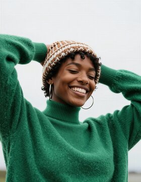 Una mujer sonr&iacute;e con alegr&iacute;a, con un gorro tejido y un jersey verde esmeralda.