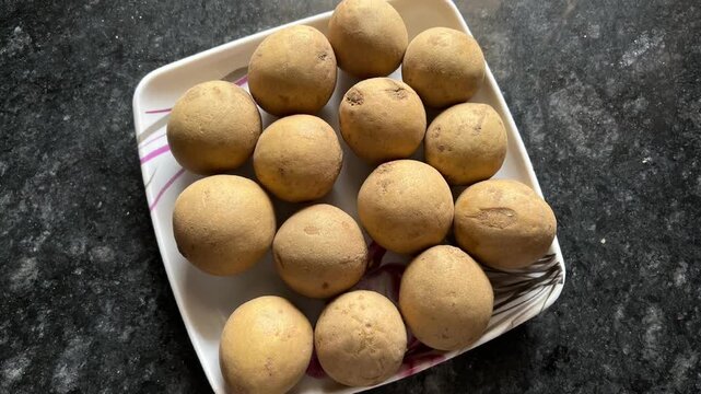 Fresh whole sapodilla fruits (Chiku) served on a white square plate