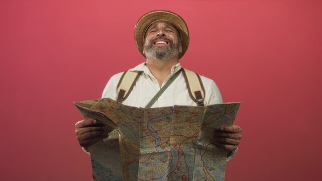 Man holding unfolded map and gripping its edges, wearing pith helmet and backpack straps in a red studio setting; curiosity travel discovery.