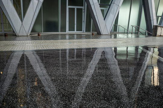 Modern corporate architecture structure pattern with reflection on wet ground in empty urban space of La Defense Paris district