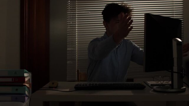 Stressed man sitting at a desk in a dark office at night, furious at an unresponsive computer screen while working overtime, exhausted and overwhelmed by deadlines and burnout