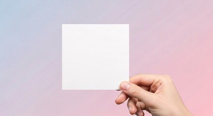 Obraz premium Close-up of a hand holding a square white card mockup over a vibrant yet soft pink and purple gradient background, ideal for feminine branding.