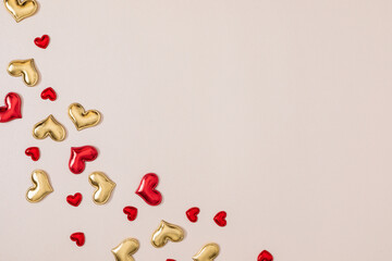Romantic background with red and gold decorative hearts on beige surface. Concept for Valentine's Day, weddings, or holiday greetings with space for text. Top view. Flat lay.