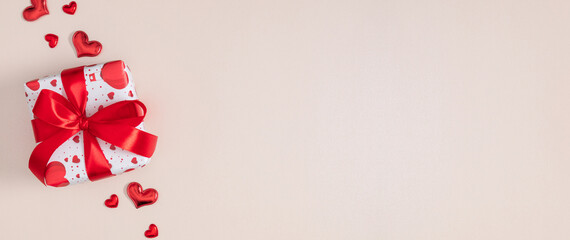 Valentine's Day banner: Gift box with red ribbon and hearts on beige background. Romantic flat lay for wedding, anniversary, or Mother's Day with wide copy space. Top view, minimalist concept.