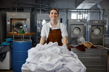 Female worker pushes a cart full of white sheets in a laundromat