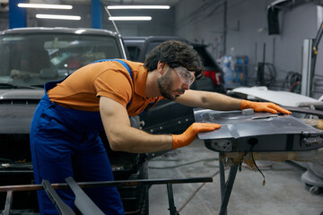 Auto technician sanding car body panel with orange gloves in workshop