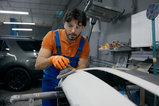 Auto body technician sanding car panel in workshop - repair and refinishing process