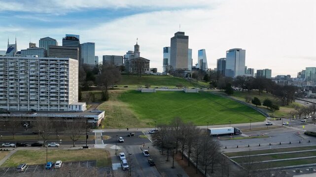 Aerial flyover shot of busy road in Nashville, green grass on hills and famous skyline skyscrapers of downtown in distance. Peaceful sunrise in the morning. Wide shot.