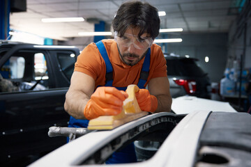 A mechanic is sanding a car bumper in an automotive garage specializing in bodywork
