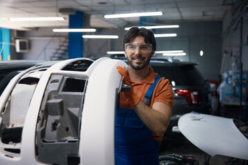 Smiling automotive technician holding car bumper in garage