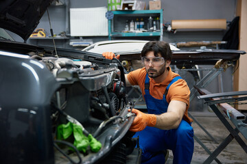 Automotive mechanic repairing car in professional garage with safety goggles and gloves