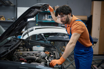 Auto mechanic inspecting car engine under the hood in garage