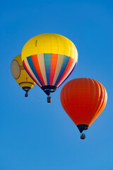 Fototapeta premium Three colorful hot air balloons with brightly colored envelopes and balloonists in the baskets hanging below on a sunny day in the Sauerland region (Germany), set against a cloudless blue sky. 