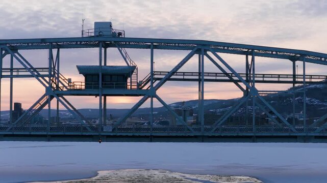 Close-up side profile of the Duluth Aerial Lift Bridge steel truss at sunset with traffic crossing.