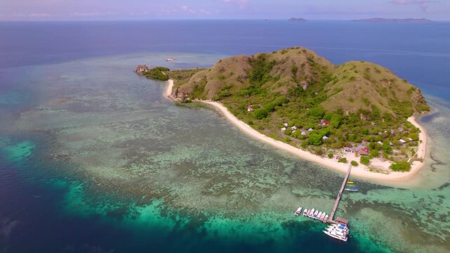 Orbital aerial revealing Kanawa Island, a small tropical island surrounded by crystal-clear turquoise waters and coral reefs in Komodo National Park, Indonesia.