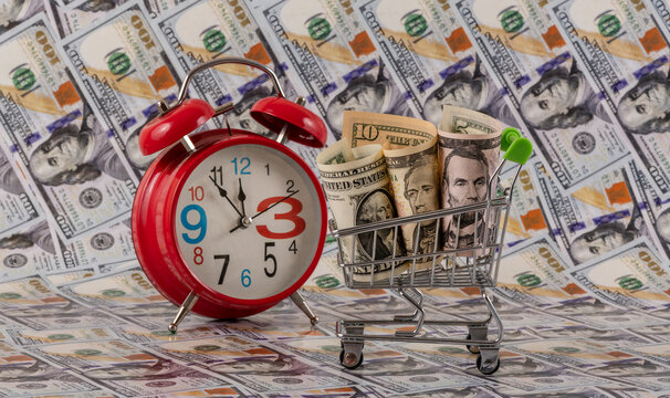 US $1, $5 and $10 bills in a miniature shopping cart with $100 bills in the background