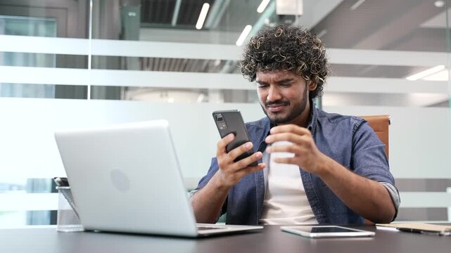 Worried disappointed businessman having problems with software or service on mobile phone smartphone sitting at workplace in business office. Frustrated man complains about bad internet connection