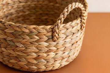 Obraz premium Close-up of a handcrafted seagrass basket with braided rope handles on a neutral terracotta background. Concept of sustainable home decor, natural eco-friendly materials and bohemian interior style.