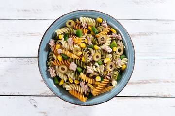 Pasta salad with tuna, corn and olives in bowl on white wooden table