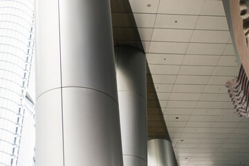 Obraz premium Several large steel columns rise to support a high ceiling inside a modern building. Natural light comes in through big glass windows nearby