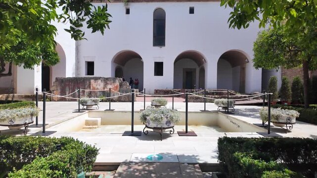 Visitor gracefully walks between tall, manicured hedges in the historic Patio de Crucero gardens at Alc&aacute;zar de los Reyes Cristianos palace, Cordoba, Spain.
