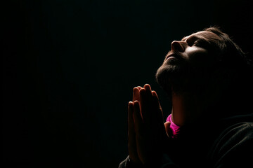 Young man praying in darkness with folded hands