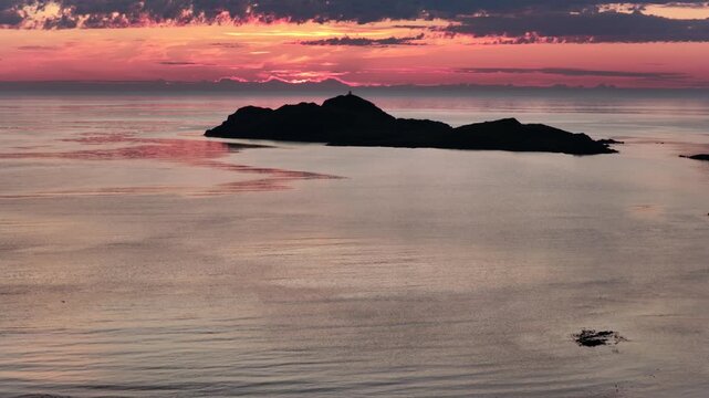 backward drone flight above sea at Ramberg, midnight sun in summer. Cloudy night, beautiful coastline, small island with lighthouse, mountains in background. midnight sun in arctic Norway. Amazing nat