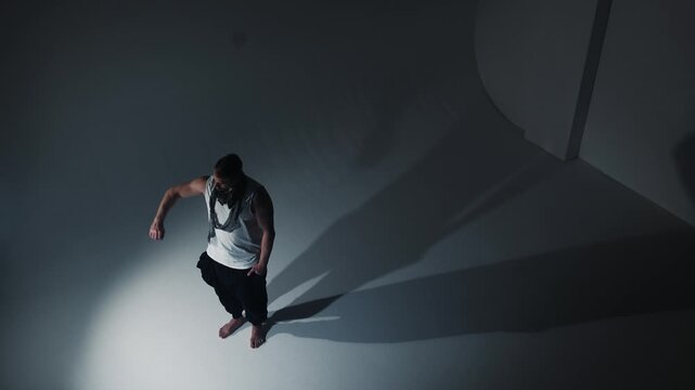 In a minimalist setting with stark, angled light, a contemplative young man is captured as his figure splits into two sharp shadows on the white expanse, symbolizing the duality inherent in human natu